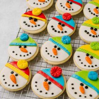 12 sugar cookies, decorated as snowmen, on a cooling rack.
