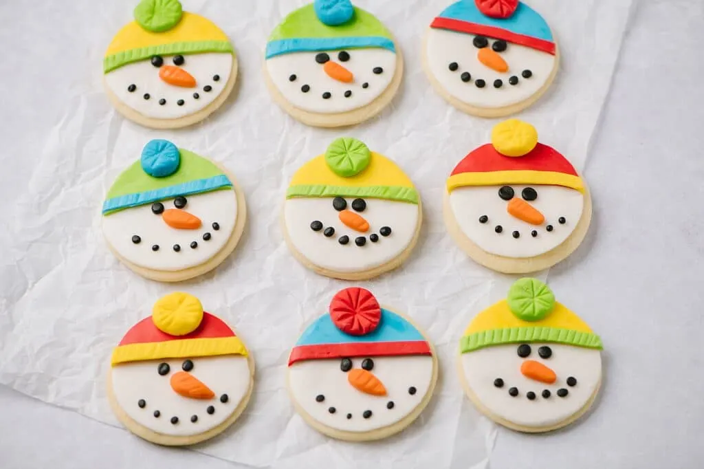 Nine sugar cookies shaped like snowmen faces, with different colored hats.