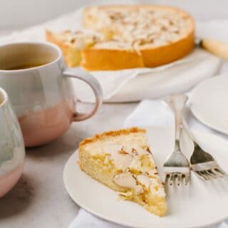 A slice of swedish visiting cake, with two mugs and the larger cake in the background.