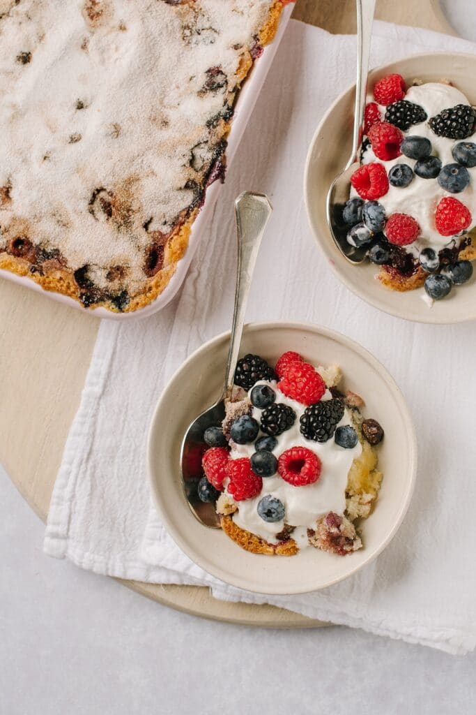 Berry Cobbler with Cinnamon Crunch Topping in two bowls with the pan in the background