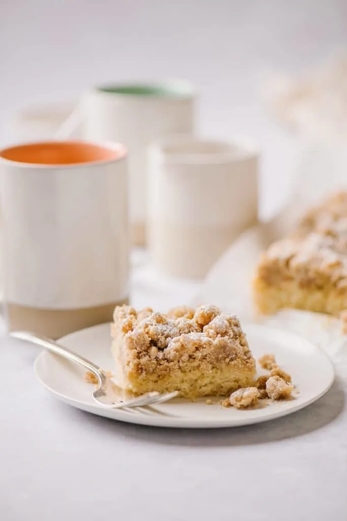 new york style crumb cake on a plate with cups of coffee in the background