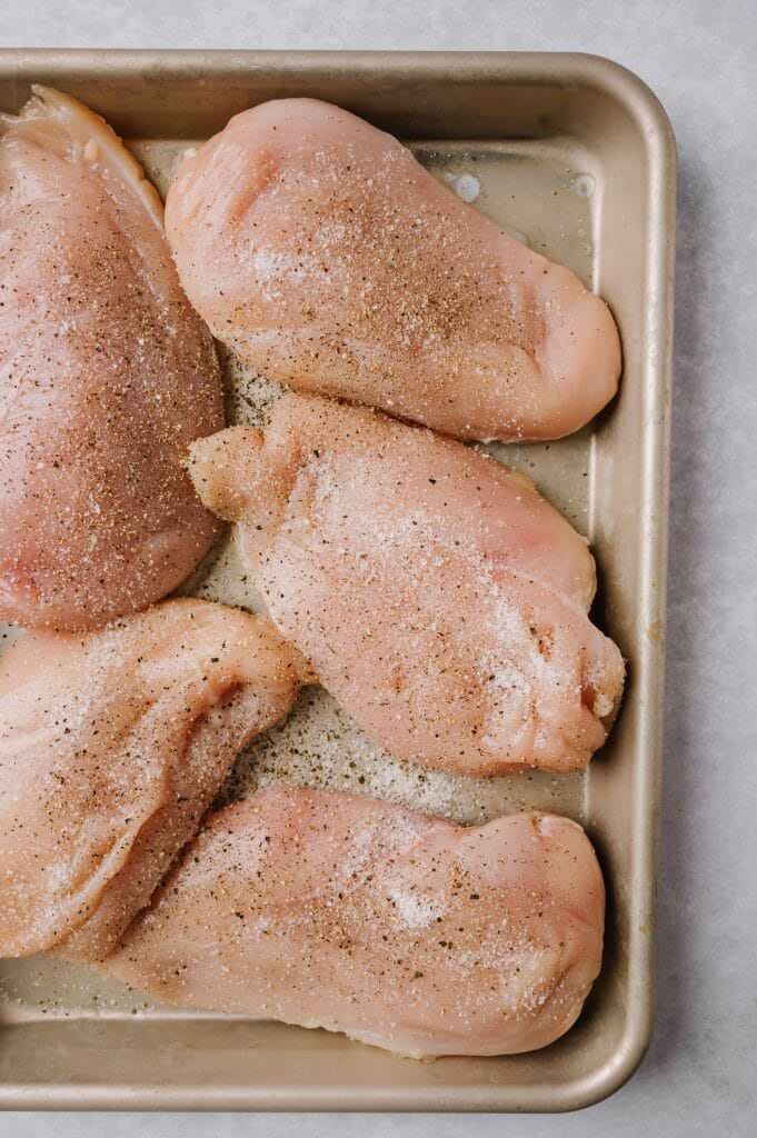 chicken breasts with salt and pepper on a sheet pan