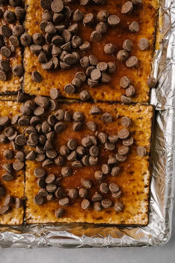 chocolate chips on hot salted matzah toffee on a foil lined baking sheet