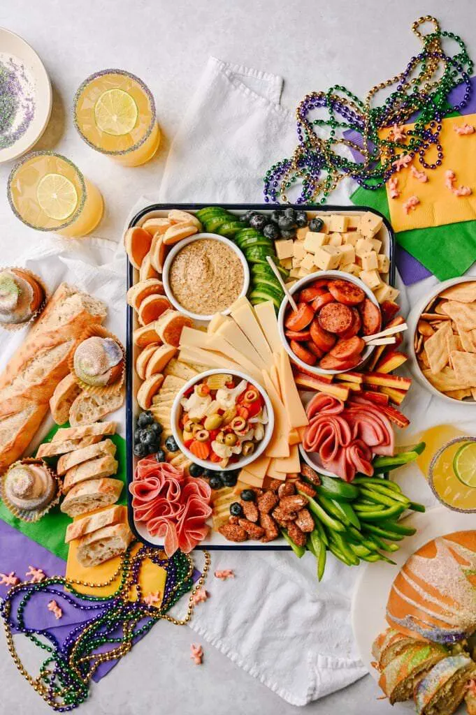 Mardi Gras-Inspired Cheeseboard with mardi gras beads king cake french bread and yellow green and purple napkins around it