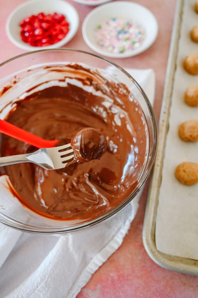 peanut butter balls being dipped into melted chocolate on a fork