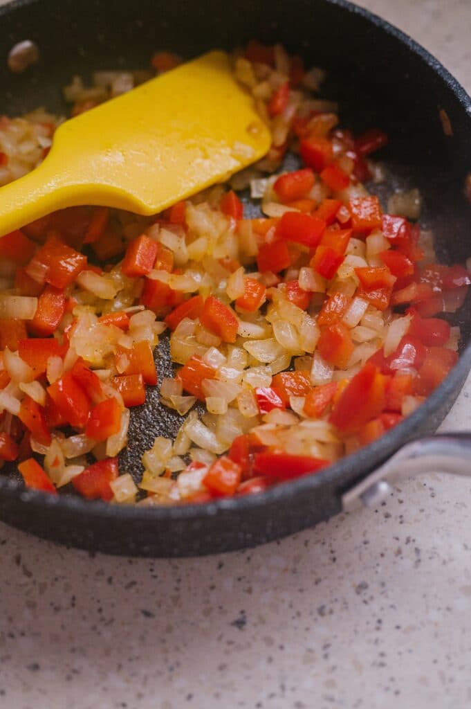 red peppers and onions being sauteed in a pan