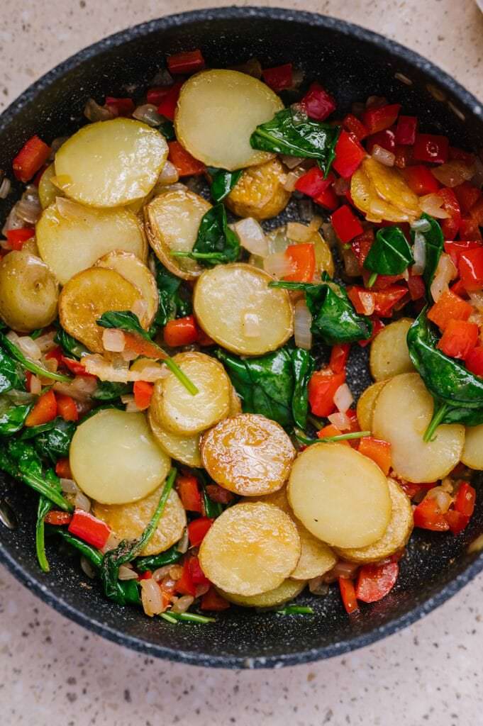 potatoes, peppers, onions, and spinach sauteed in a pan