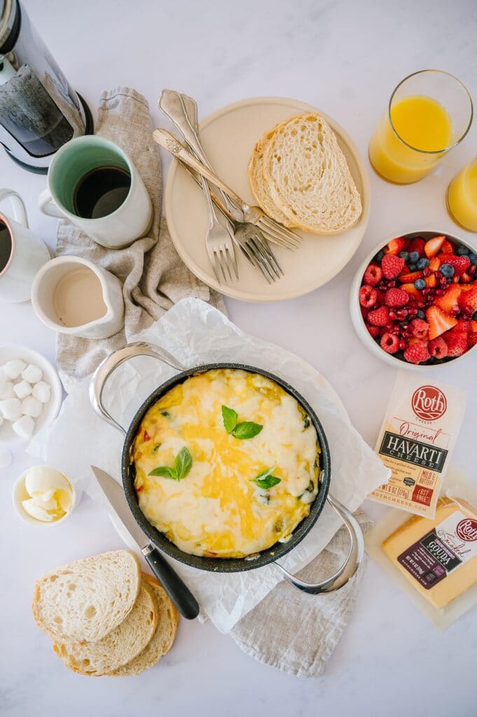 baked frittata in a pan with cheese, berries, orange juice, toast, and coffee around it.