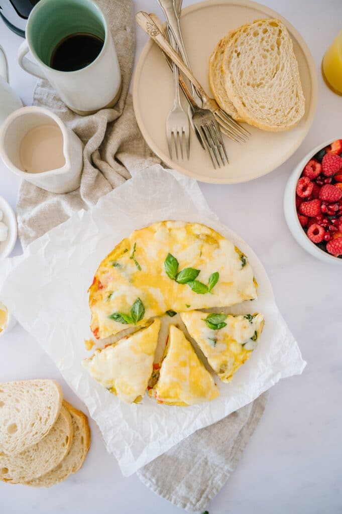 baked frittata sliced on a platter with berries, coffee, and toast around it
