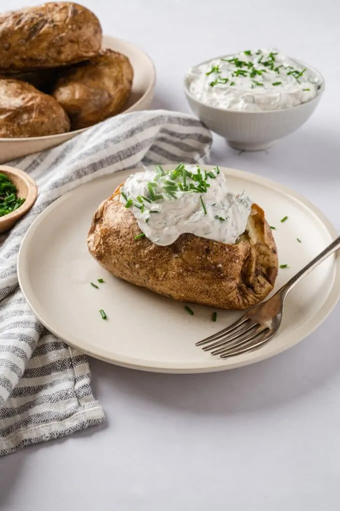 baked potato on a plate with sour cream and chives