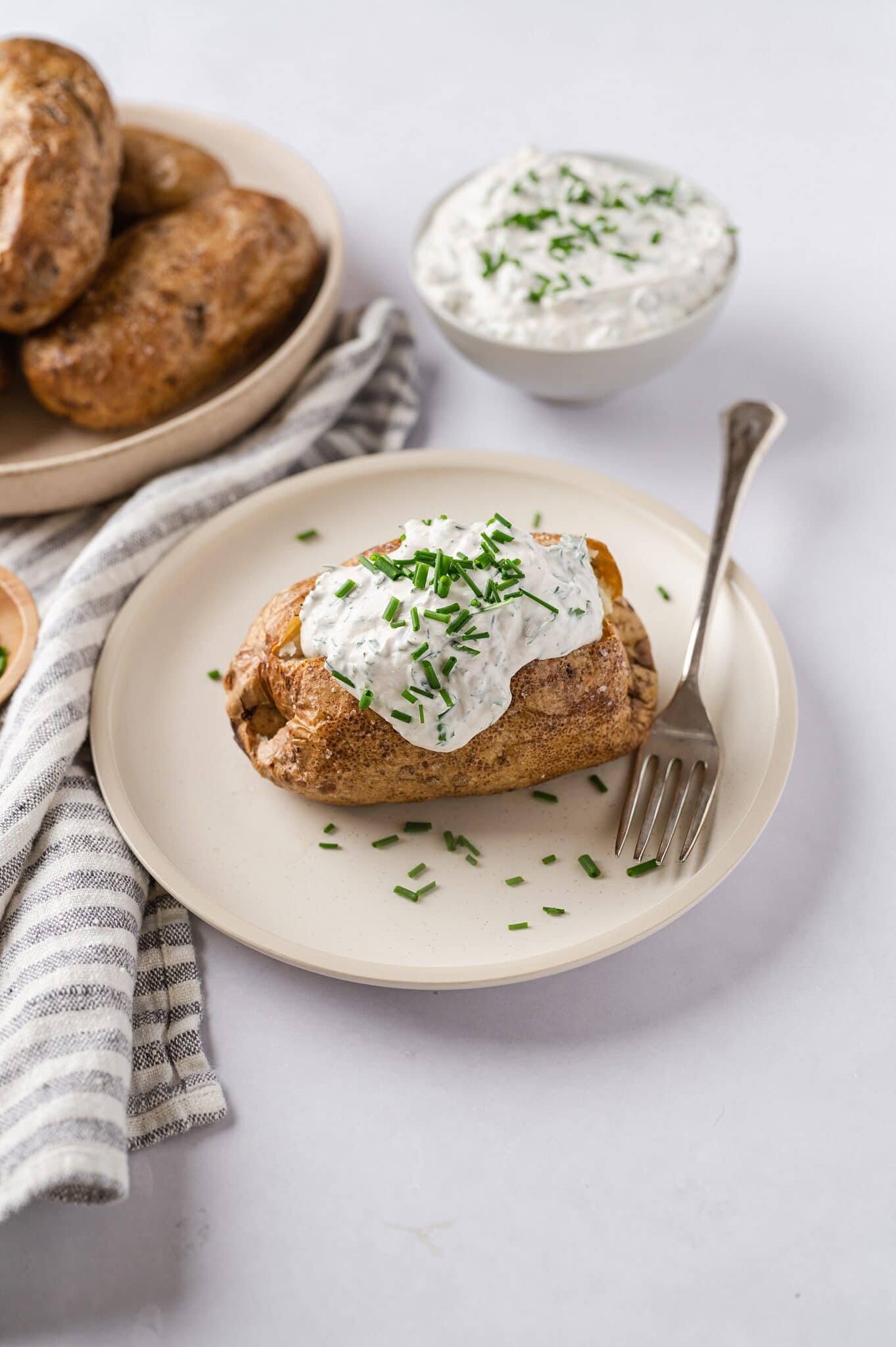 baked potato with sour cream and chives on a plate with baked potatoes, sour cream and chives in the background