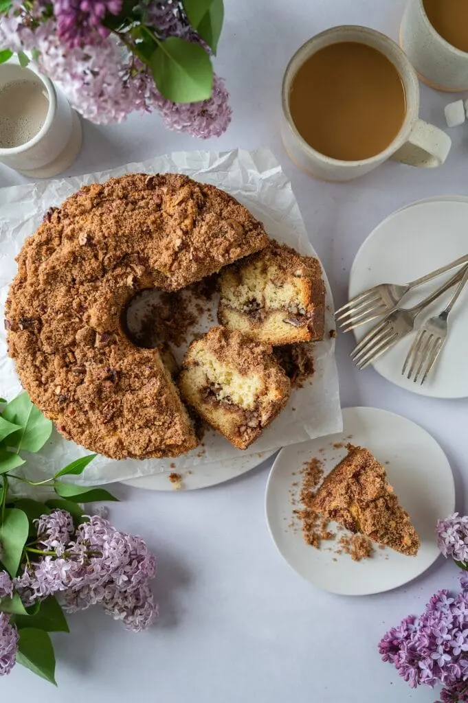 sliced coffee cake with full cake and a cup of coffee in the background