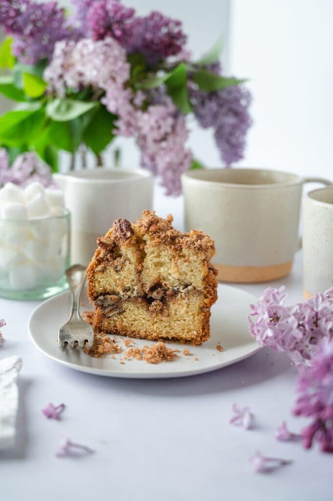 slice of blue ribbon coffee cake on a plate with cup of coffee and flowers in the background