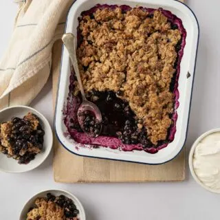 two bowls of gluten free blueberry crisp with full dish behind