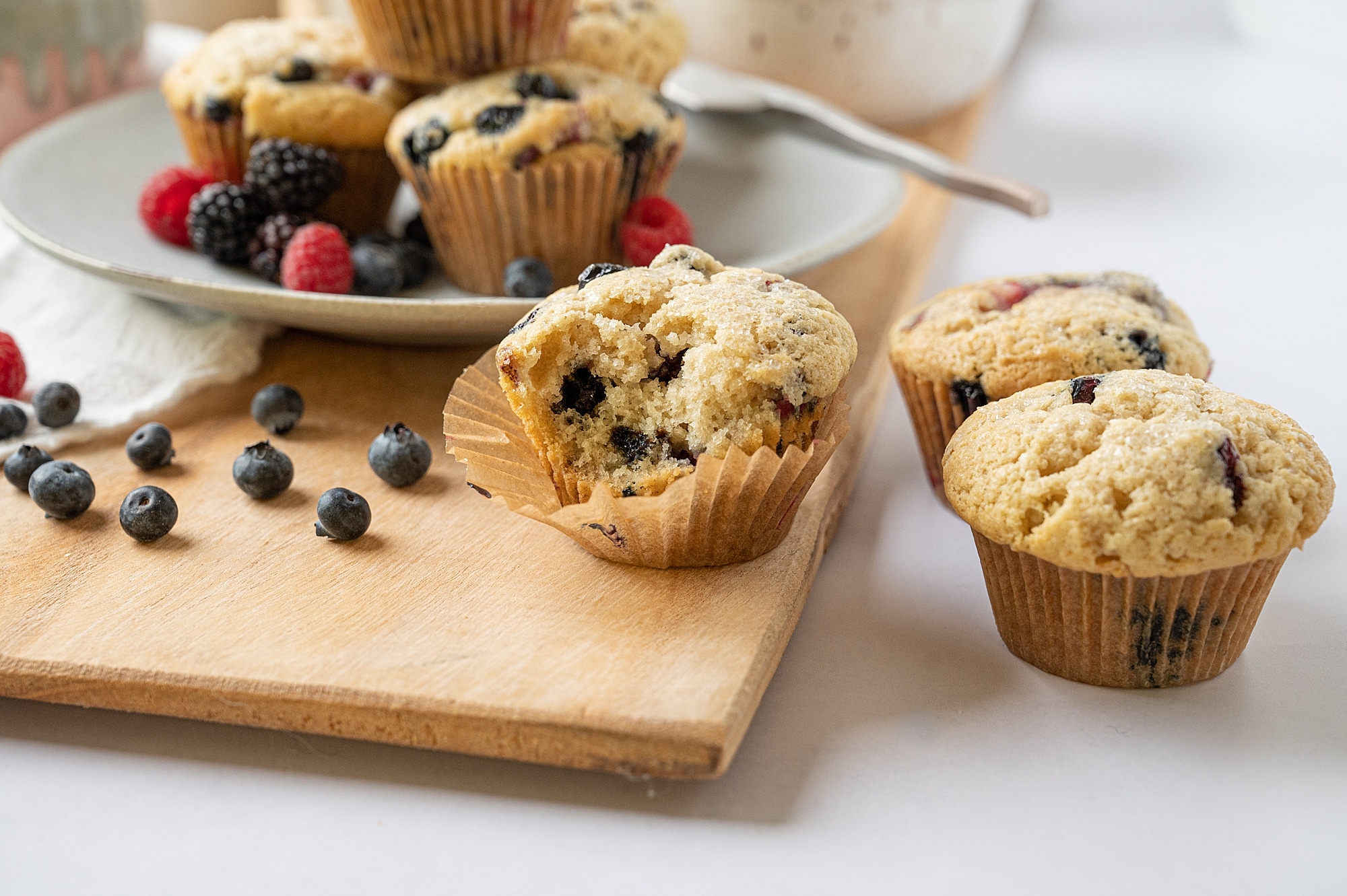 vegan vanilla berry muffin on a cutting board with berries and a plate of muffins