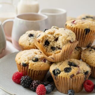 plate of vegan vanilla berry muffins with coffee cups and a bowl of berries in the background