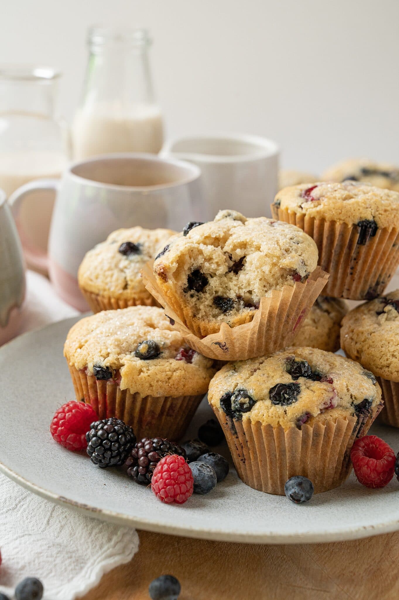 plate of vegan vanilla berry muffins with coffee cups and a bowl of berries in the background