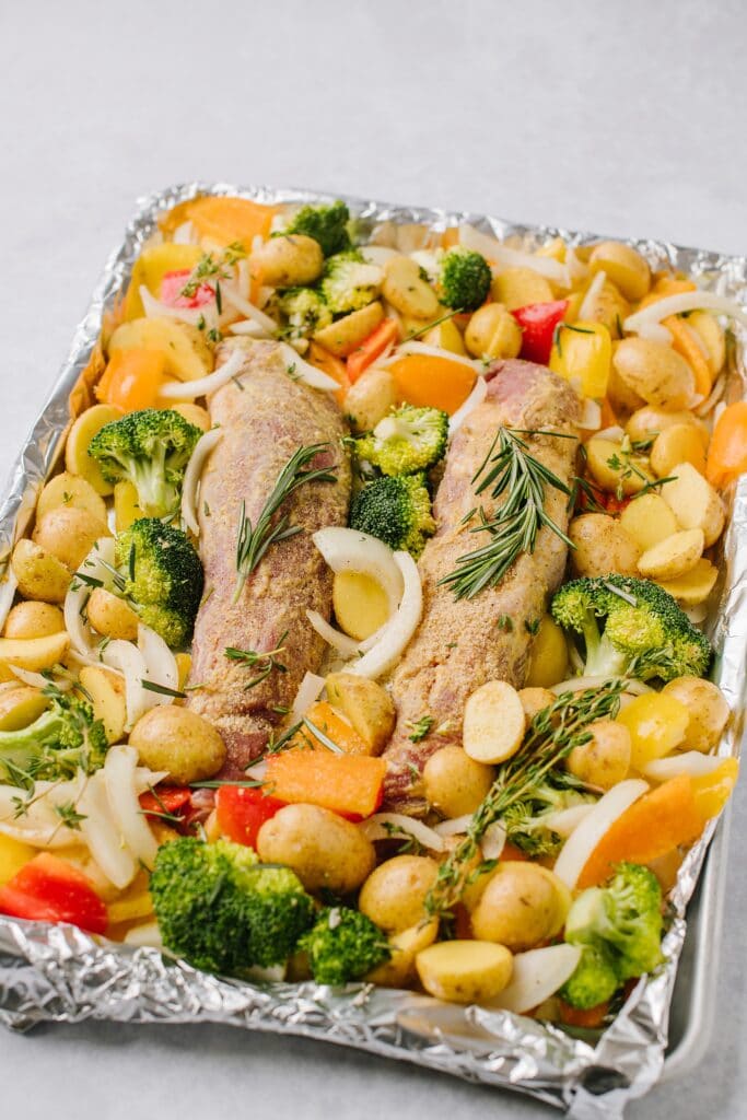 seasoned pork, veggies and potatoes on a sheet pan ready for the oven